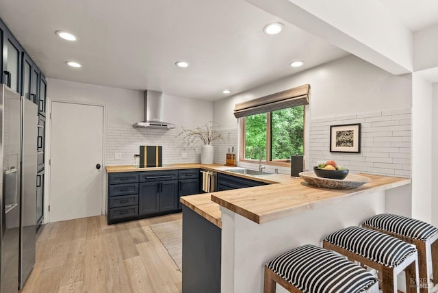 269 Castro St, Lagunitas, CA 94938 - kitchen with butcher block counters, a peninsula, wall chimney range hood, light wood-type flooring, and a sink