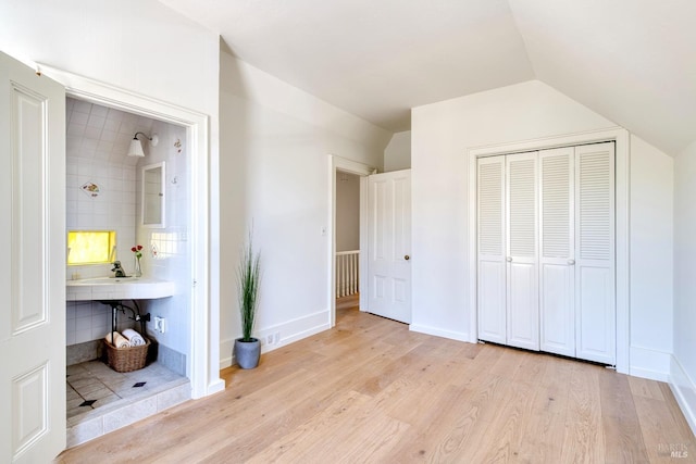 unfurnished bedroom featuring baseboards, a closet, lofted ceiling, light wood-style floors, and ensuite bathroom