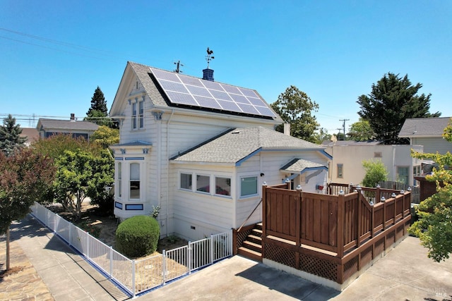 rear view of house featuring crawl space, roof with shingles, a wooden deck, fence private yard, and roof mounted solar panels