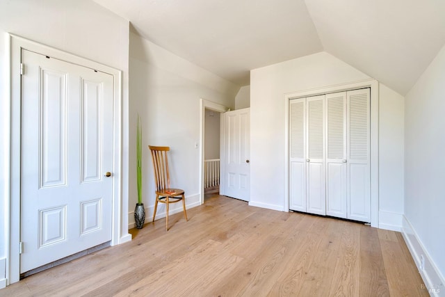 unfurnished bedroom featuring light wood-style floors, baseboards, lofted ceiling, and a closet