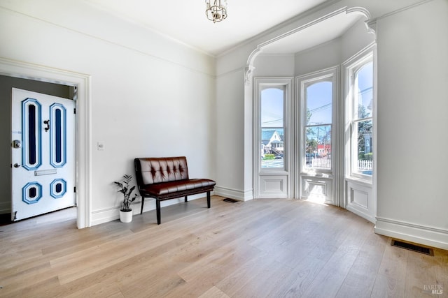 sitting room featuring baseboards, visible vents, ornamental molding, and light wood-style floors