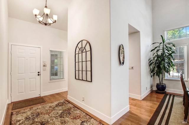 foyer with a high ceiling, a chandelier, baseboards, and light wood-style floors