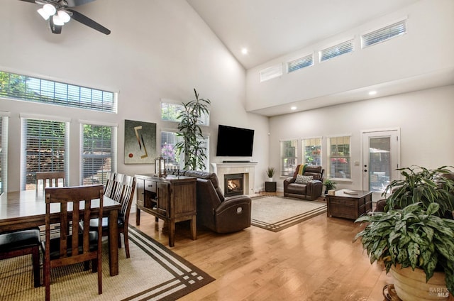 living area featuring high vaulted ceiling, a glass covered fireplace, a healthy amount of sunlight, and light wood-style flooring
