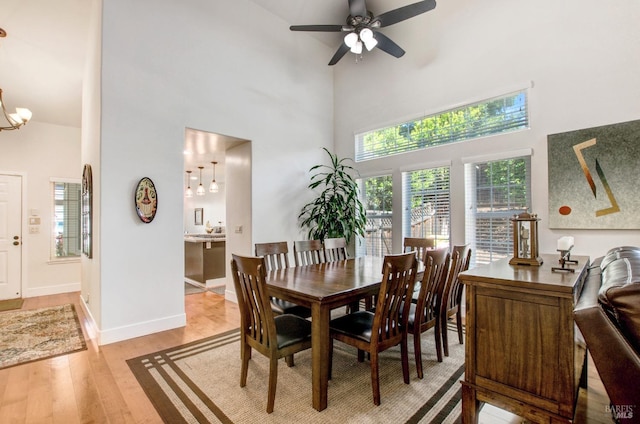 dining room featuring light wood-style floors, baseboards, ceiling fan with notable chandelier, and a high ceiling