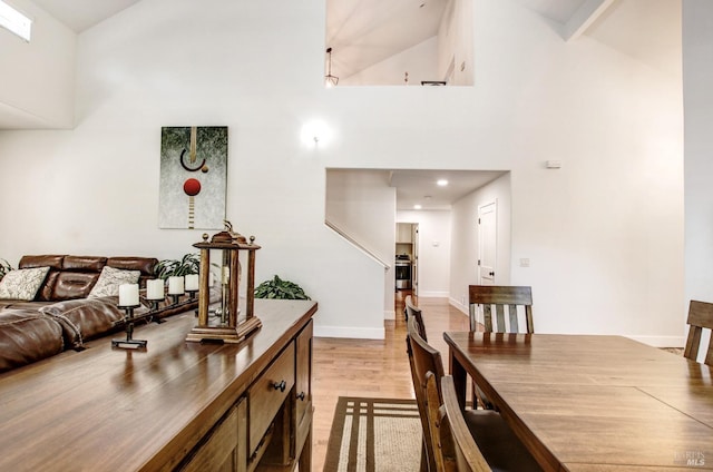 dining area featuring light wood-style floors, high vaulted ceiling, and baseboards