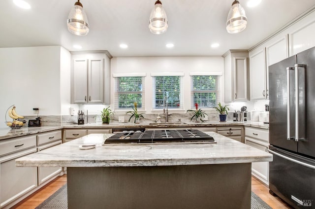 kitchen featuring a sink, appliances with stainless steel finishes, a center island, and light stone counters