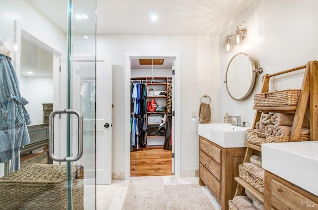 full bathroom featuring a walk in closet, a stall shower, vanity, baseboards, and recessed lighting