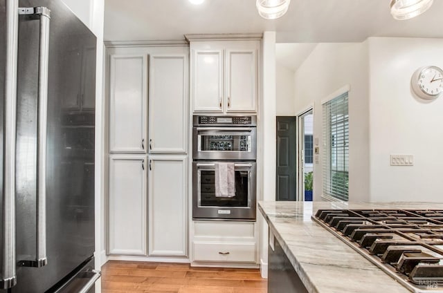kitchen with white cabinets, stainless steel appliances, light stone countertops, and light wood finished floors