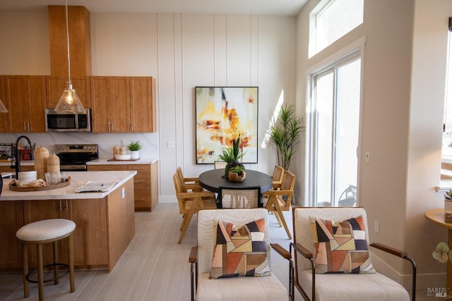 kitchen with brown cabinetry, a towering ceiling, a breakfast bar, light countertops, and appliances with stainless steel finishes