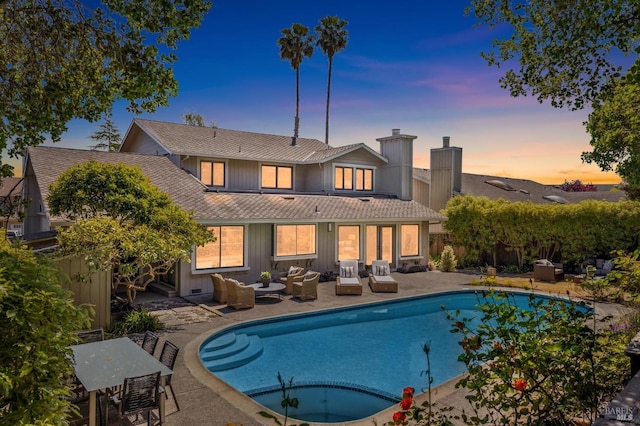 back of house at dusk featuring fence, outdoor lounge area, an outdoor pool, a chimney, and a patio area
