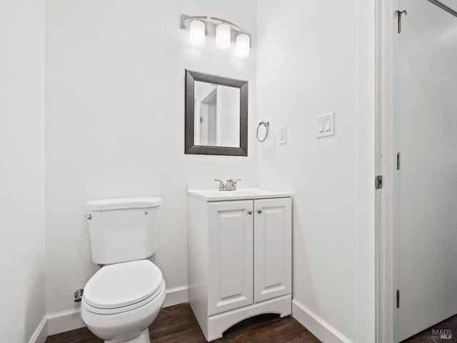 half bath featuring baseboards, vanity, toilet, and wood finished floors