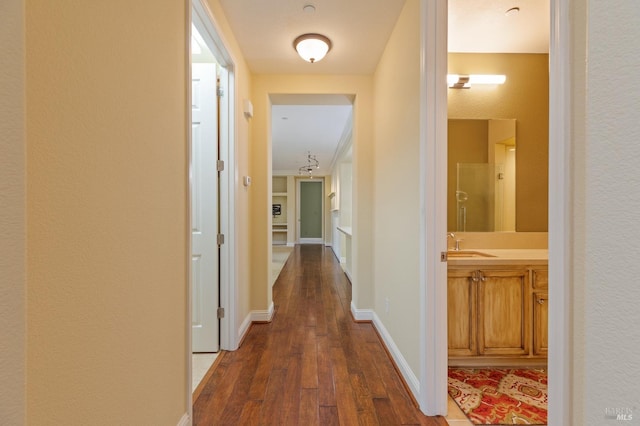 hall with a sink, baseboards, and dark wood-style flooring