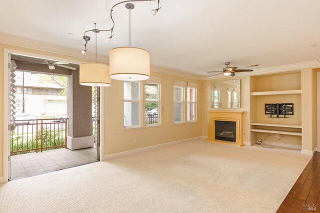 unfurnished living room with crown molding, a ceiling fan, built in features, and a glass covered fireplace