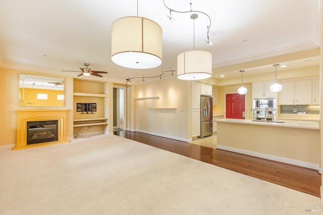 unfurnished living room with crown molding, a sink, light wood-style floors, and a ceiling fan