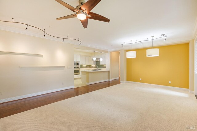 unfurnished living room featuring crown molding, ceiling fan, light carpet, a sink, and baseboards