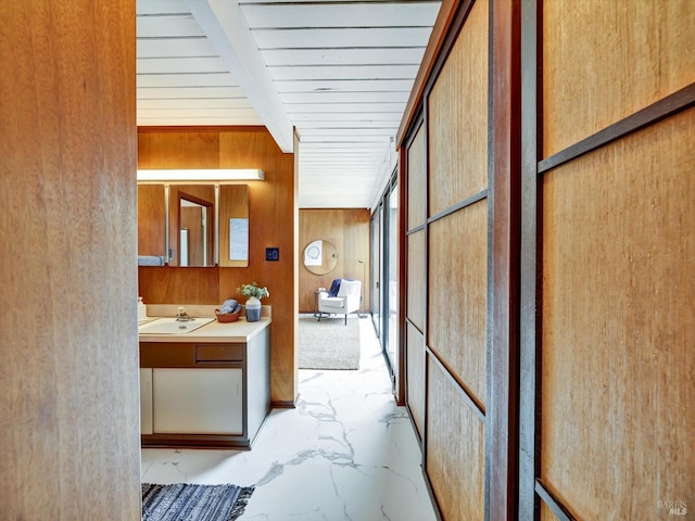 corridor with a sink, marble finish floor, and wooden walls