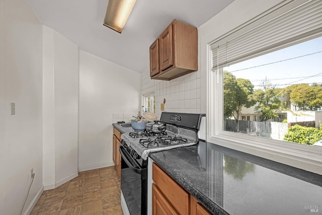 kitchen with gas stove, brown cabinetry, stone finish floor, baseboards, and tasteful backsplash