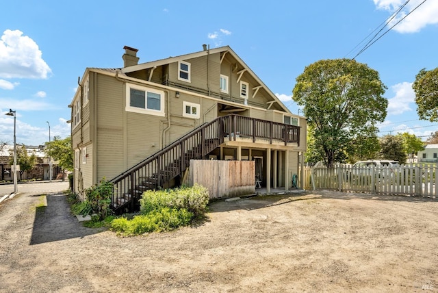 rear view of property with fence, a wooden deck, a chimney, and stairway
