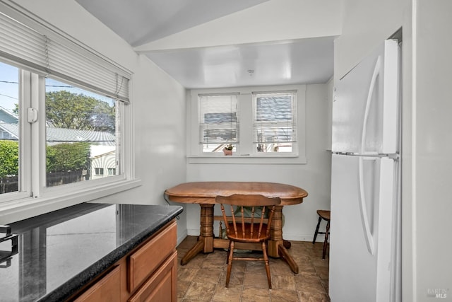 dining space with baseboards, stone finish flooring, plenty of natural light, and vaulted ceiling