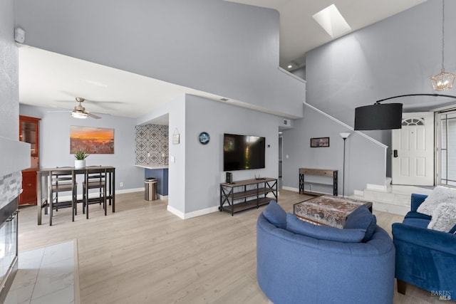 living room featuring light wood-type flooring, baseboards, ceiling fan, and a high ceiling
