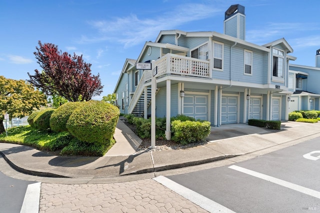 view of side of home featuring stairs, a chimney, an attached garage, and driveway