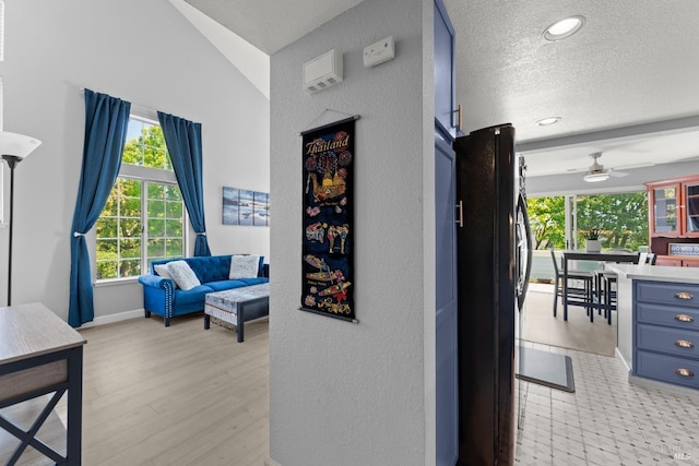 corridor featuring a textured ceiling, baseboards, light wood finished floors, a textured wall, and recessed lighting