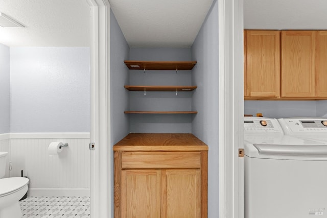 laundry area featuring visible vents, a textured ceiling, a wainscoted wall, separate washer and dryer, and cabinet space