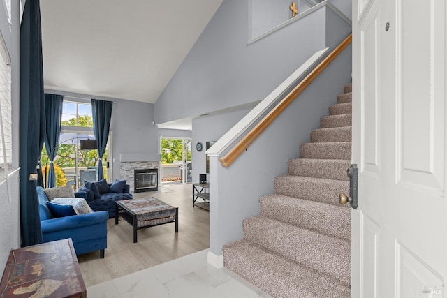 stairs featuring marble finish floor, a glass covered fireplace, and high vaulted ceiling