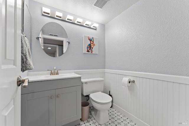 bathroom with visible vents, wainscoting, vanity, tile patterned floors, and toilet