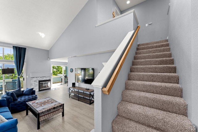 staircase with a fireplace with flush hearth, high vaulted ceiling, and wood finished floors