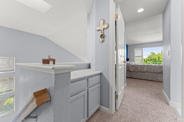 hall with baseboards, light carpet, and vaulted ceiling with skylight