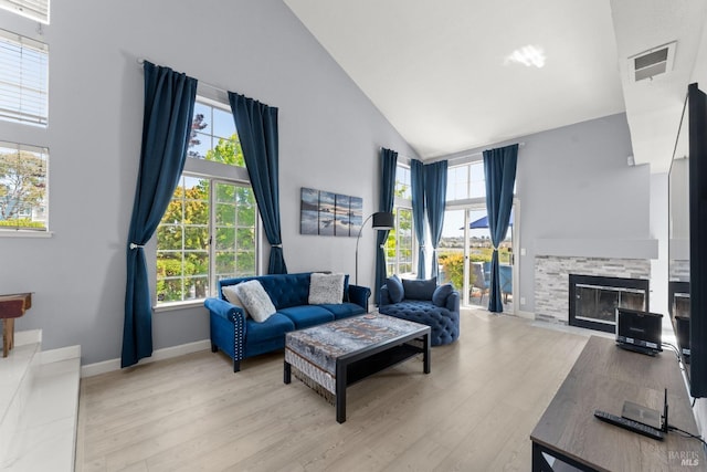 living area with a stone fireplace, visible vents, wood finished floors, high vaulted ceiling, and baseboards