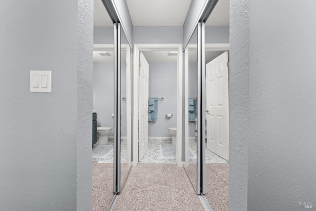 corridor with carpet floors, a textured wall, and visible vents