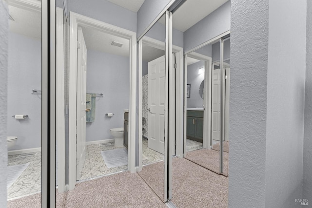 bathroom with toilet, a textured wall, and visible vents