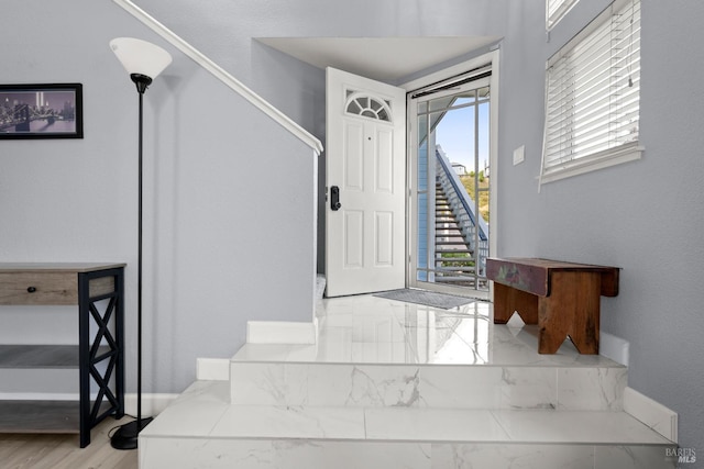 foyer entrance featuring baseboards, marble finish floor, stairs, and a wealth of natural light