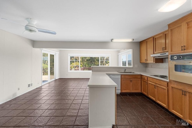kitchen with light countertops, a sink, a peninsula, under cabinet range hood, and white appliances