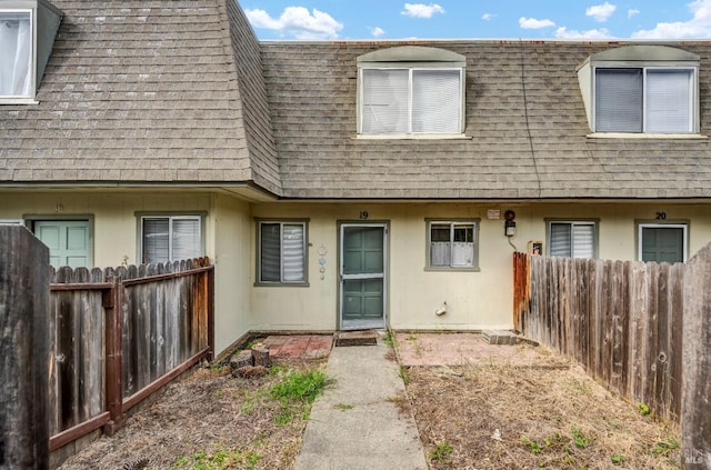 property entrance with a shingled roof, fence, and mansard roof