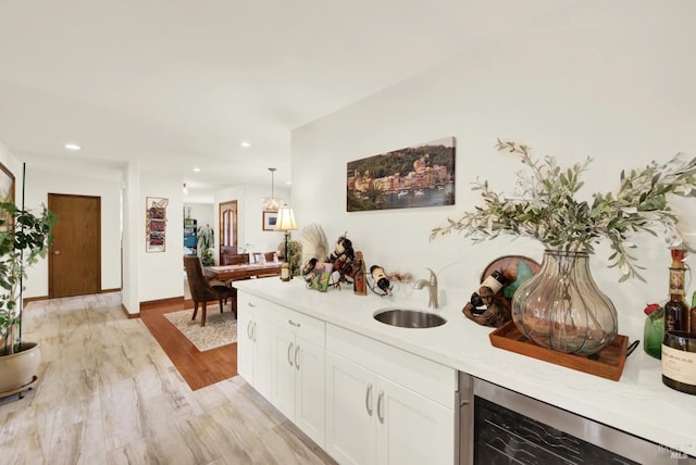 bar featuring a sink, recessed lighting, light wood finished floors, and beverage cooler