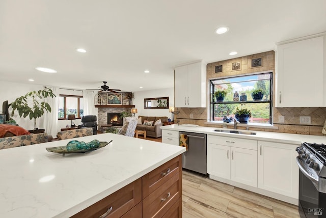 kitchen with ceiling fan, a sink, dishwasher, a stone fireplace, and open floor plan