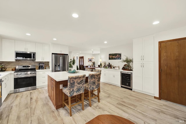kitchen featuring appliances with stainless steel finishes, light wood finished floors, beverage cooler, a kitchen breakfast bar, and a center island
