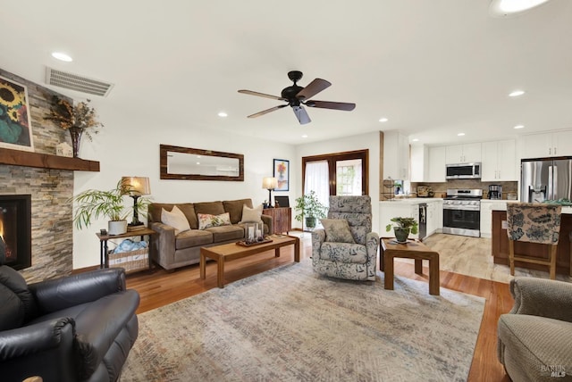 living area with visible vents, a stone fireplace, recessed lighting, light wood-type flooring, and a ceiling fan