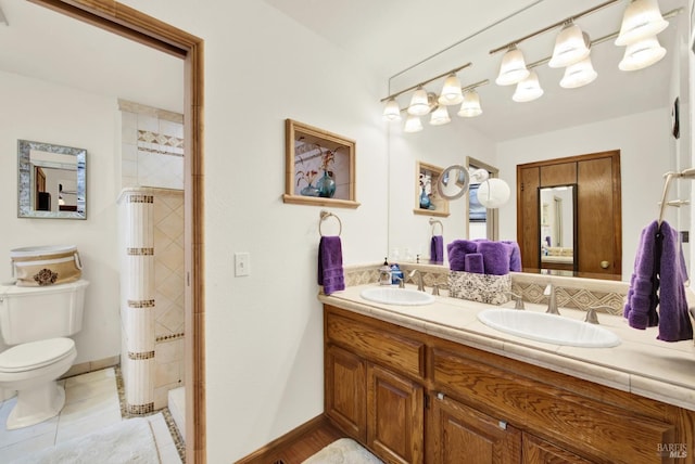 bathroom with double vanity, toilet, a tile shower, and a sink