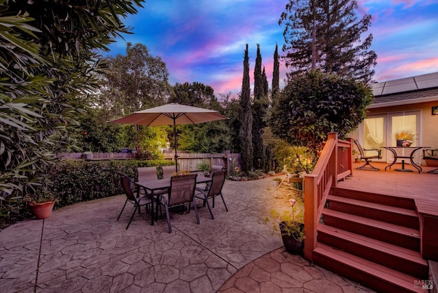 patio terrace at dusk featuring fence, a wooden deck, and outdoor dining space