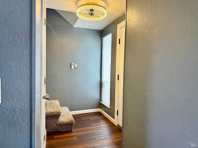 hallway featuring dark wood-style flooring, baseboards, a textured wall, and a healthy amount of sunlight