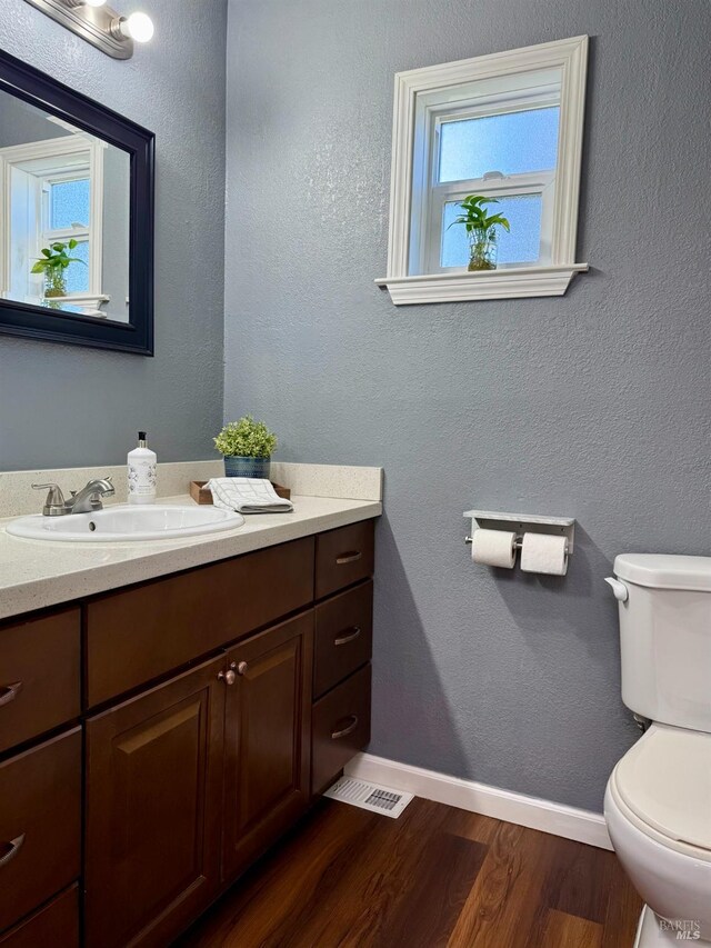 bathroom with vanity, visible vents, wood finished floors, toilet, and baseboards