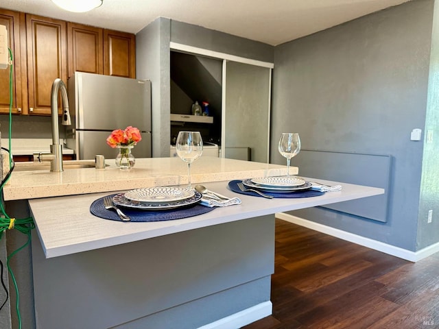 kitchen featuring brown cabinetry, freestanding refrigerator, baseboards, dark wood-type flooring, and light countertops