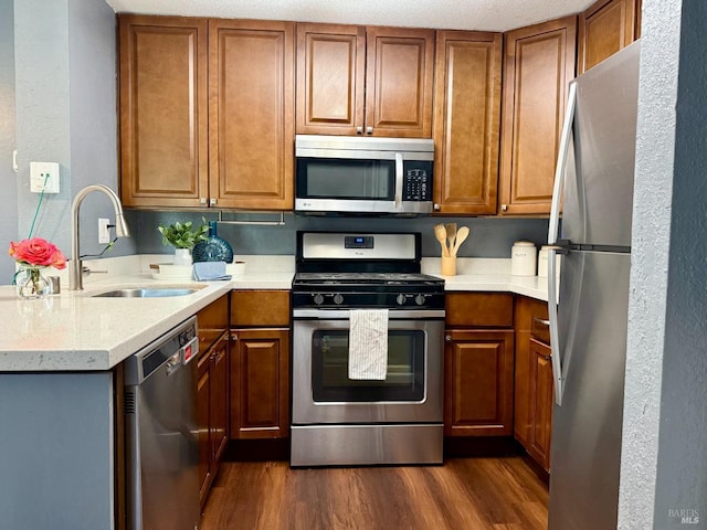 kitchen with dark wood-style floors, light countertops, brown cabinets, a sink, and stainless steel appliances