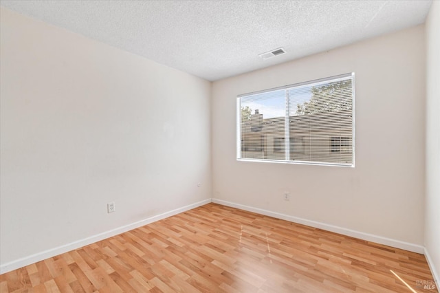 empty room with visible vents, a textured ceiling, light wood finished floors, and baseboards