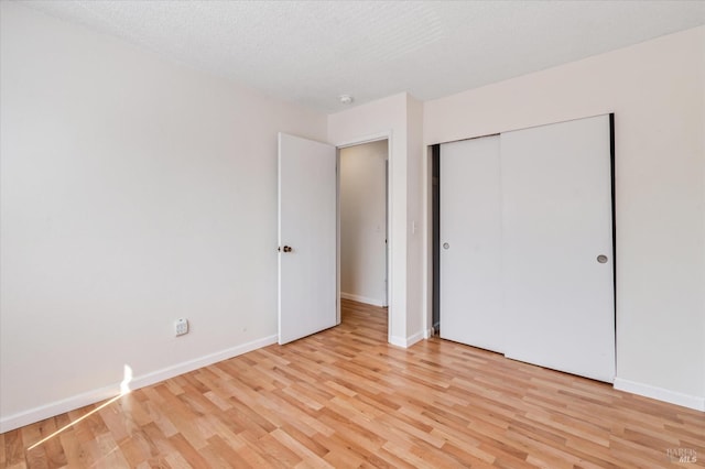 unfurnished bedroom featuring light wood-type flooring, a textured ceiling, baseboards, and a closet