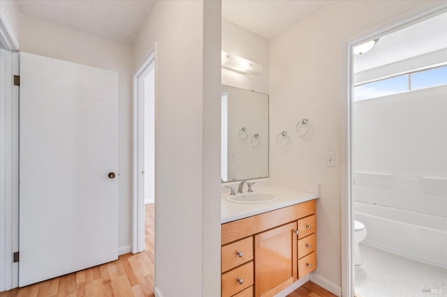 full bath featuring toilet, wood finished floors, a tub to relax in, and vanity